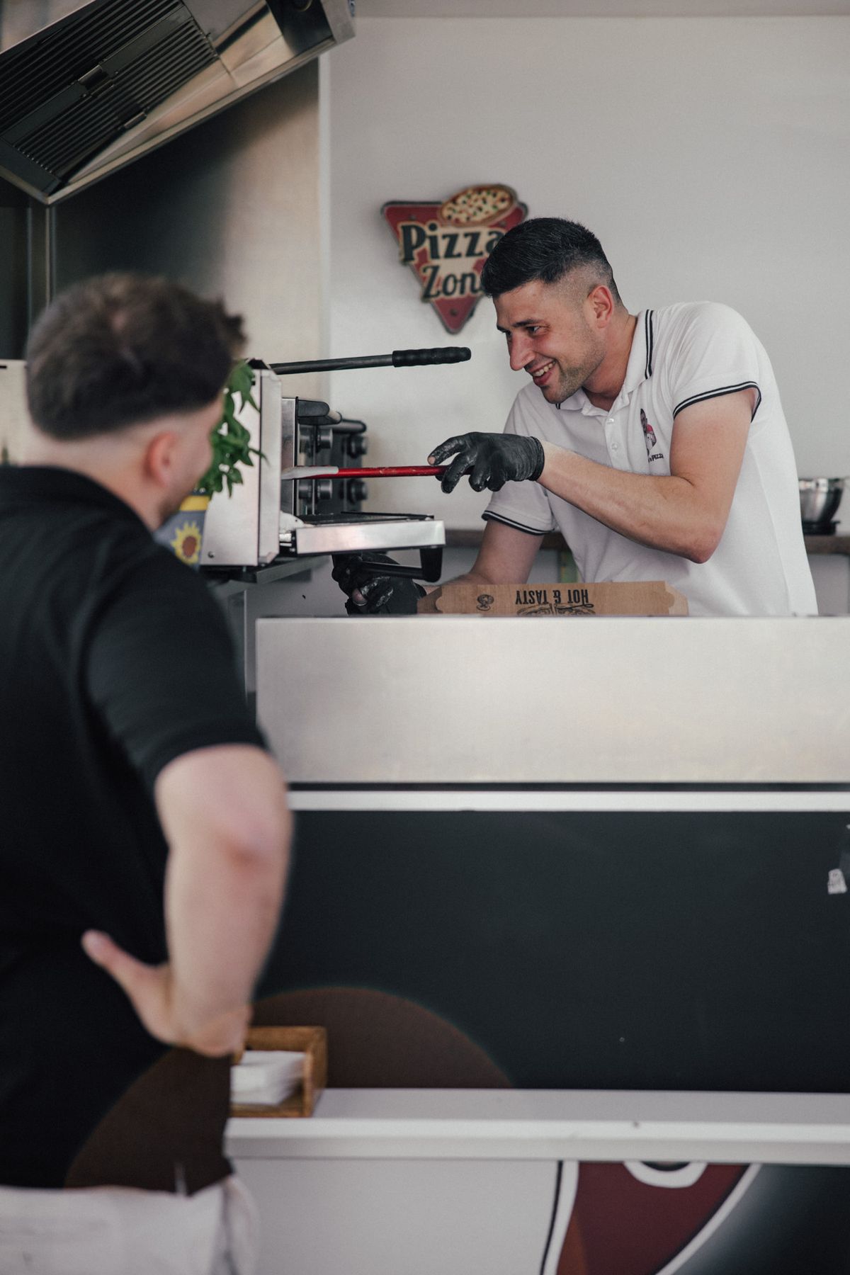 Kevin „Kevo“ Roznyak übergibt lachend eine Pizzabox am Tresen seines Food-Trailers